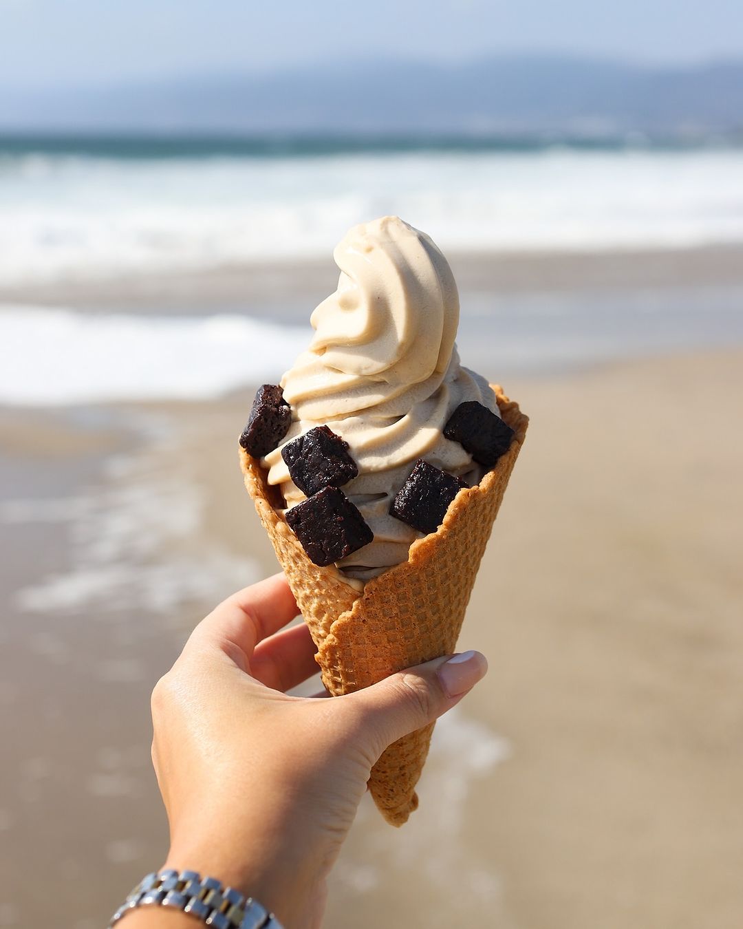 person holds soft serve in cone at beach