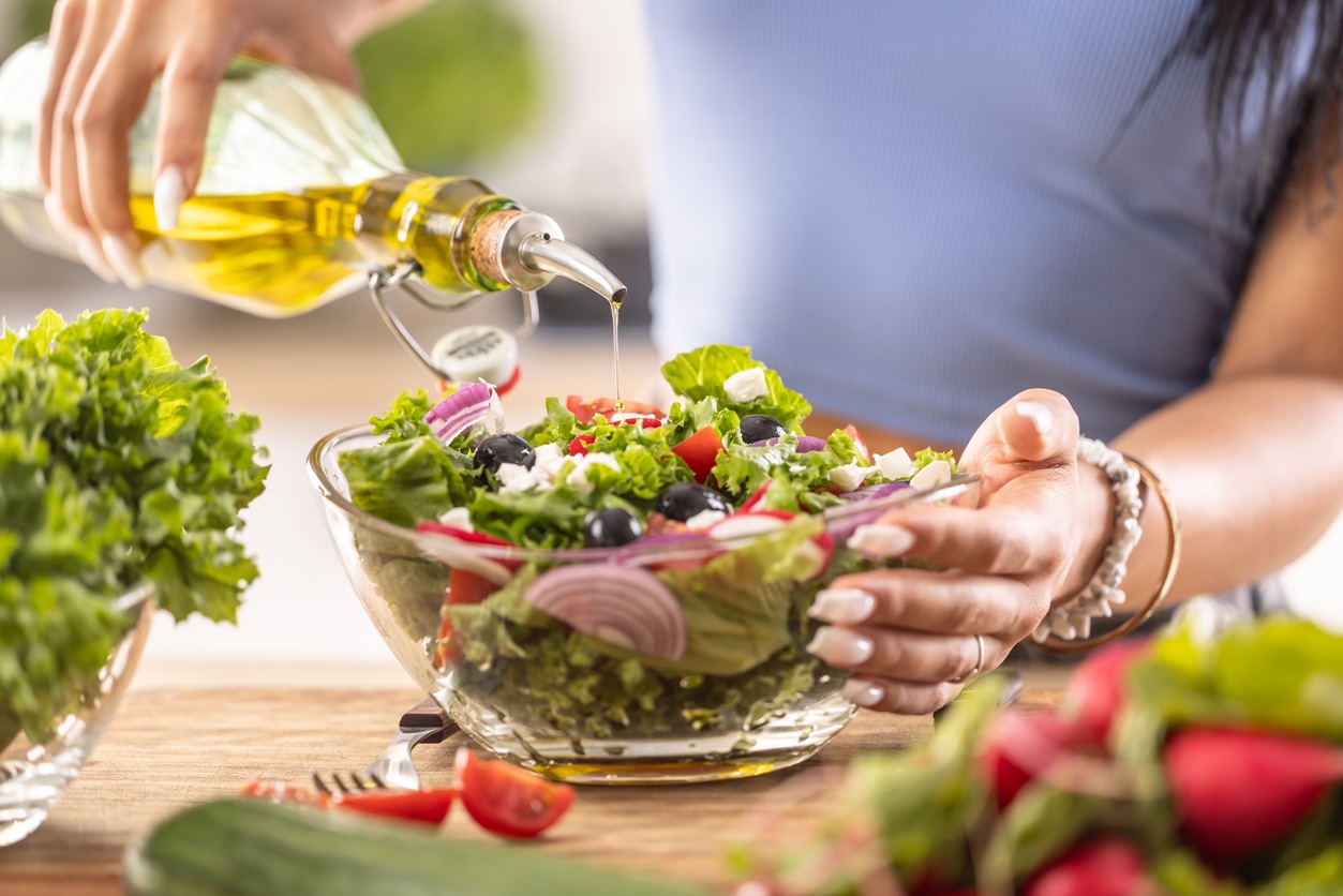 woman pours olive oil on salad