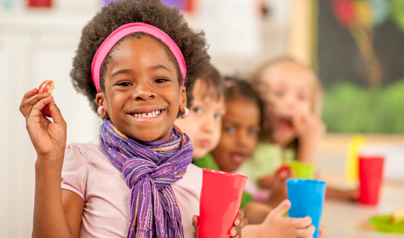 school child holds apple and cup